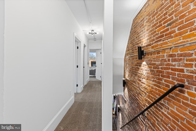 corridor featuring brick wall and dark carpet