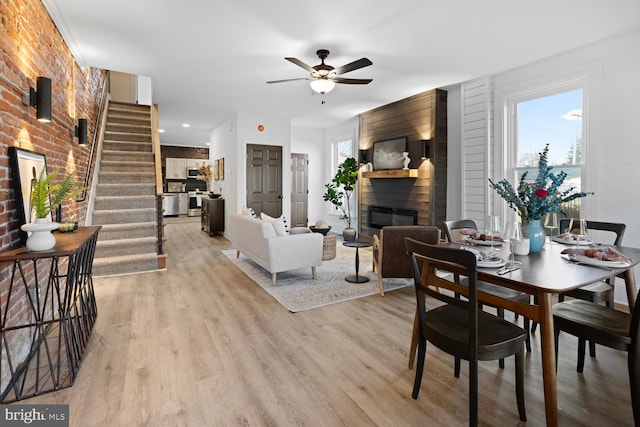 dining space featuring ceiling fan, light hardwood / wood-style floors, a fireplace, and brick wall