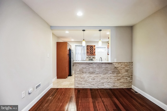 kitchen featuring kitchen peninsula, light hardwood / wood-style flooring, decorative light fixtures, stainless steel fridge, and sink