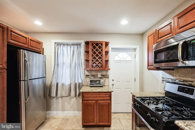 kitchen featuring light stone countertops, light tile patterned flooring, backsplash, and appliances with stainless steel finishes