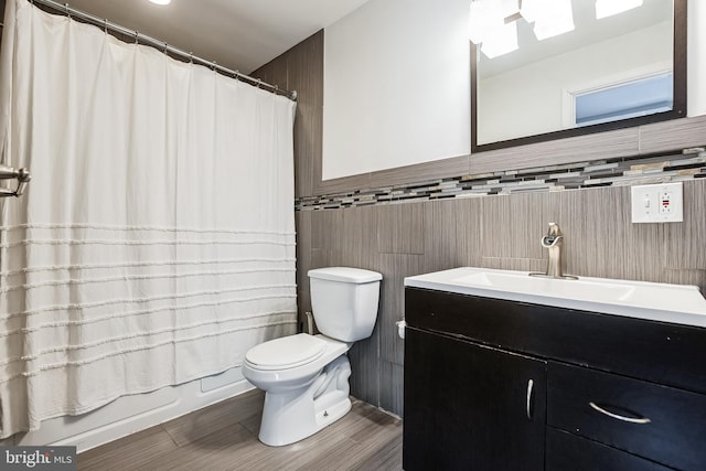 full bathroom featuring toilet, hardwood / wood-style flooring, shower / bath combo with shower curtain, tile walls, and vanity