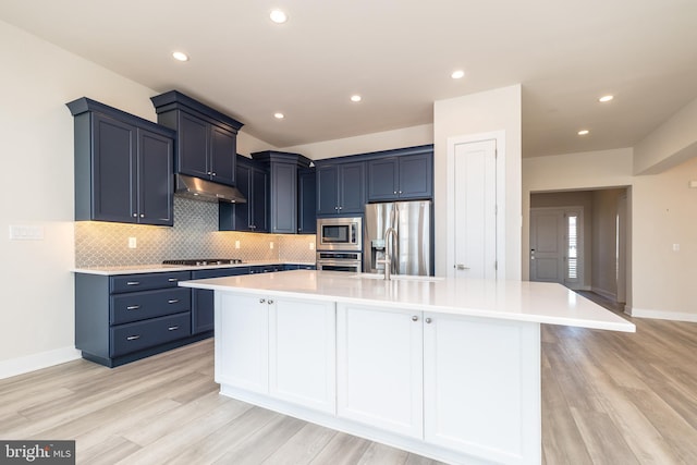 kitchen with under cabinet range hood, blue cabinetry, stainless steel appliances, and light countertops