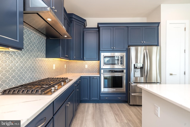 kitchen with under cabinet range hood, blue cabinets, tasteful backsplash, and appliances with stainless steel finishes