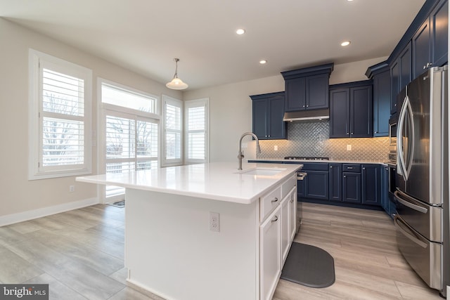 kitchen with freestanding refrigerator, a sink, light countertops, under cabinet range hood, and backsplash