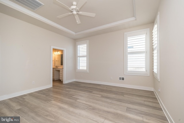 unfurnished bedroom featuring visible vents, light wood-type flooring, and a tray ceiling