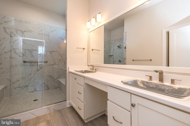 bathroom featuring double vanity, a shower stall, wood finished floors, and a sink