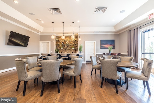 dining room with a tray ceiling, visible vents, and hardwood / wood-style floors