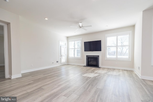 unfurnished living room with a ceiling fan, a fireplace with flush hearth, baseboards, and light wood-type flooring