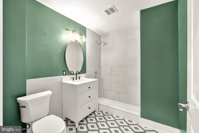 bathroom featuring vanity, toilet, tiled shower, and tile walls