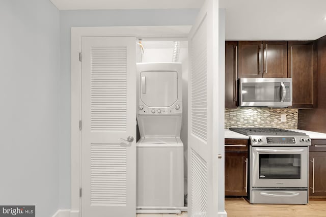 kitchen with backsplash, stacked washer and clothes dryer, light wood-type flooring, dark brown cabinets, and stainless steel appliances