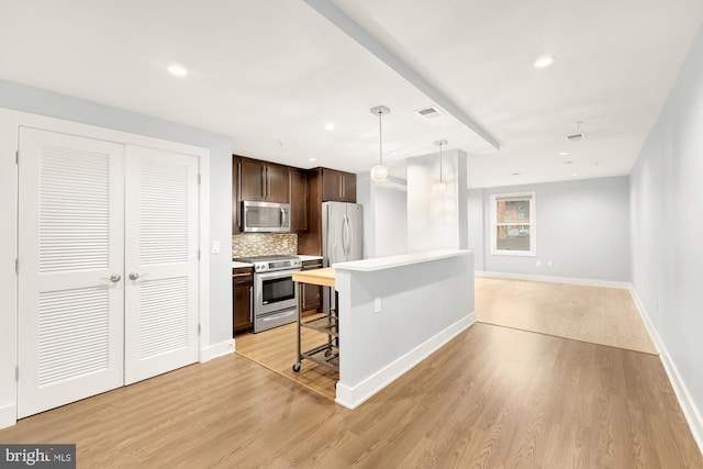 kitchen featuring a kitchen bar, appliances with stainless steel finishes, light wood-type flooring, tasteful backsplash, and decorative light fixtures