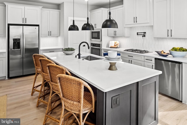 kitchen featuring a kitchen bar, a kitchen island with sink, light hardwood / wood-style floors, and appliances with stainless steel finishes