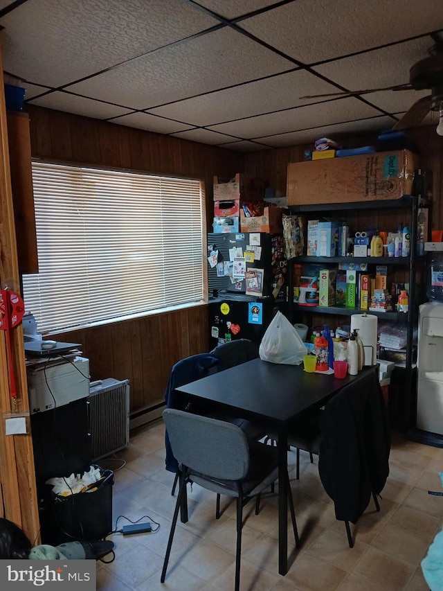 office area with a paneled ceiling, wooden walls, ceiling fan, and a baseboard heating unit