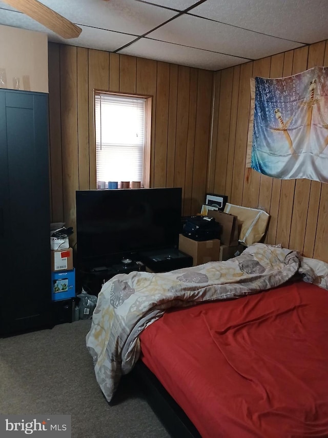 carpeted bedroom featuring a paneled ceiling and wood walls