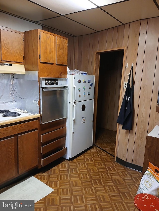 kitchen featuring dark parquet flooring, backsplash, white appliances, a paneled ceiling, and wooden walls