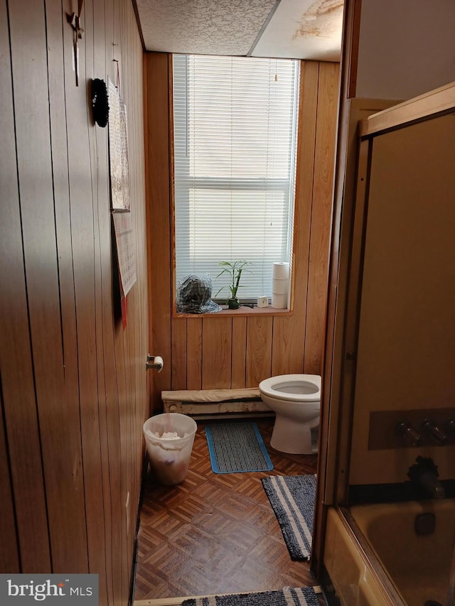 bathroom featuring toilet, parquet flooring, a textured ceiling, and wooden walls