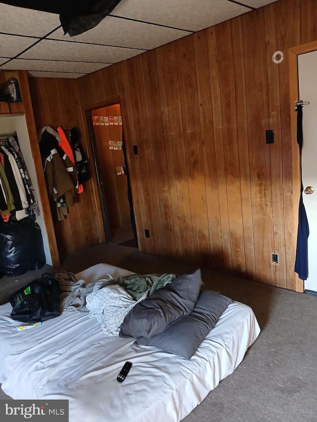 bedroom with carpet, a paneled ceiling, and wood walls