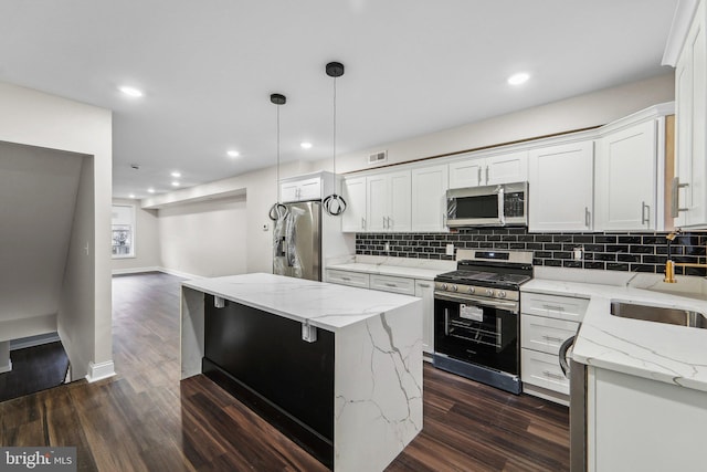 kitchen featuring light stone countertops, a center island, hanging light fixtures, stainless steel appliances, and white cabinets