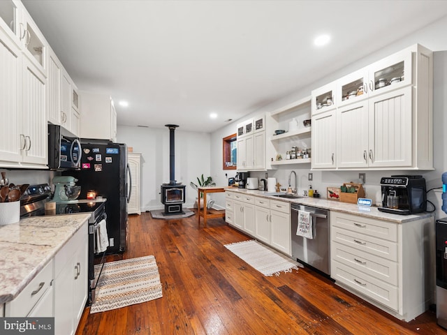 kitchen featuring appliances with stainless steel finishes, dark hardwood / wood-style flooring, light stone counters, a wood stove, and white cabinetry