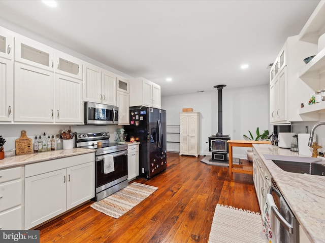 kitchen featuring a wood stove, white cabinetry, sink, and appliances with stainless steel finishes