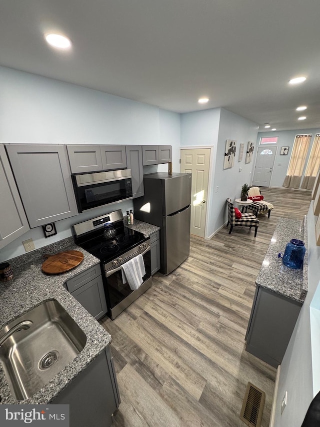 kitchen with light hardwood / wood-style flooring, stainless steel appliances, stone countertops, and sink