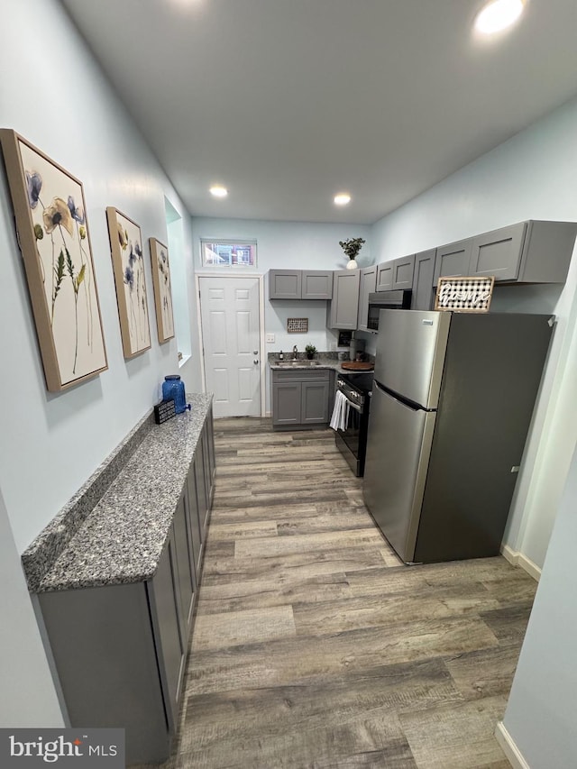 kitchen with hardwood / wood-style floors, dark stone counters, sink, gray cabinets, and stainless steel appliances