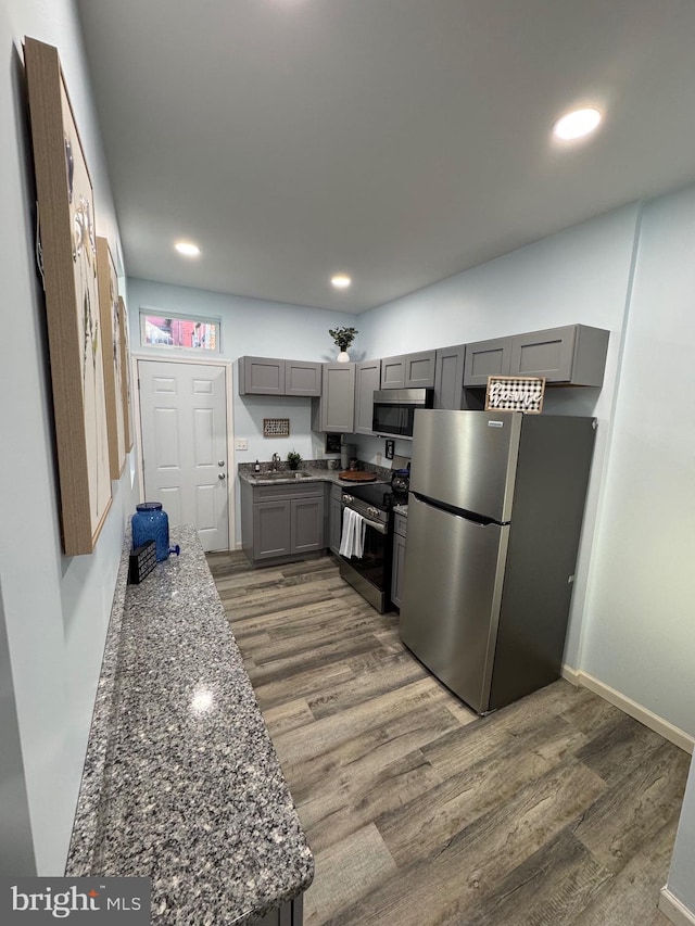 kitchen featuring stainless steel appliances, dark wood-type flooring, sink, dark stone countertops, and gray cabinets