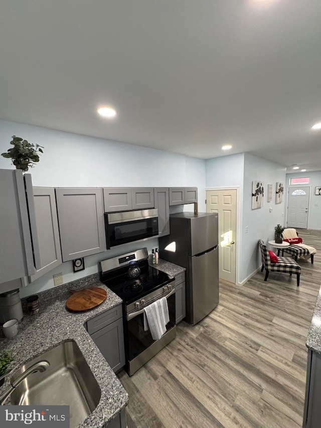 kitchen featuring gray cabinetry, sink, stainless steel appliances, light hardwood / wood-style flooring, and stone countertops