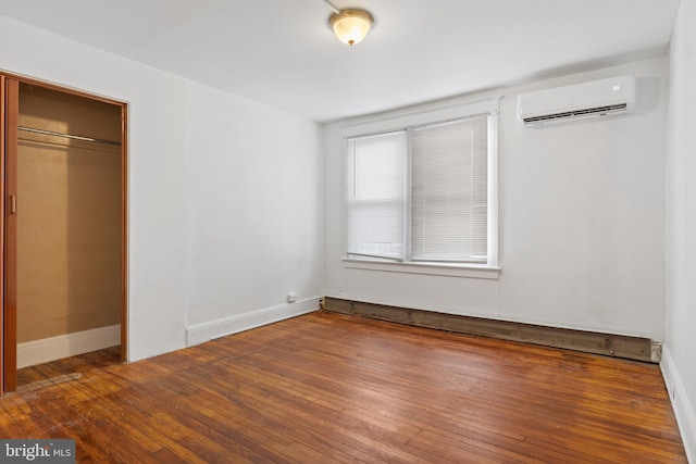 unfurnished bedroom with a closet, baseboards, wood finished floors, and a wall mounted AC