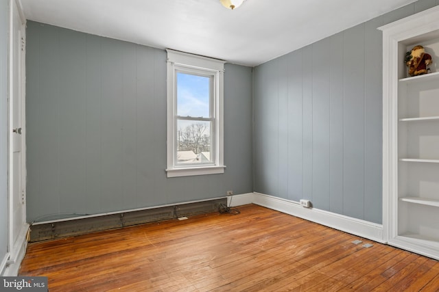 spare room with built in features, light wood-style flooring, and baseboards