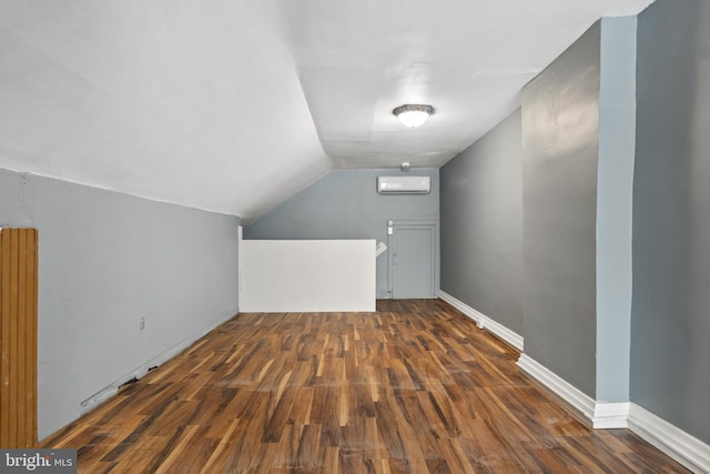 bonus room featuring dark wood-type flooring, lofted ceiling, a wall mounted air conditioner, and baseboards