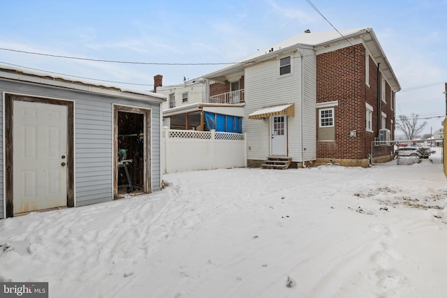 snow covered back of property featuring entry steps, fence, and brick siding