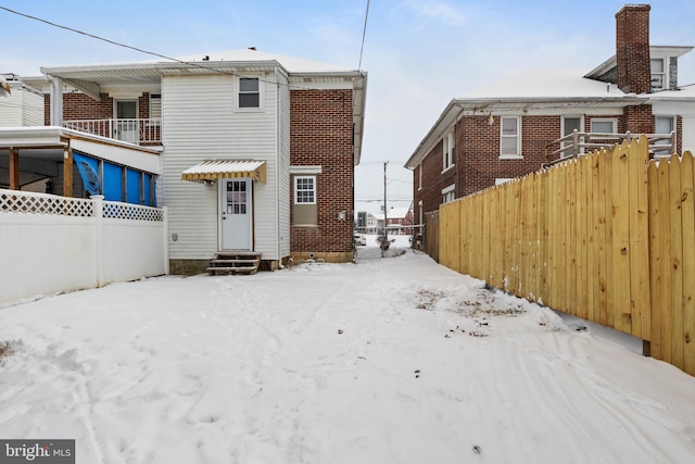 snow covered back of property with entry steps and fence