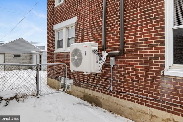 snow covered property featuring brick siding, ac unit, and fence