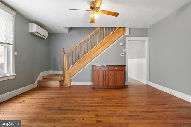 unfurnished living room featuring stairs, baseboards, dark wood finished floors, and a wall mounted air conditioner