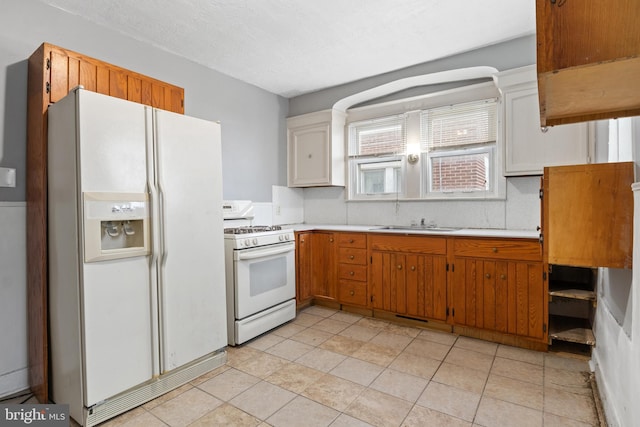 kitchen featuring a textured ceiling, white appliances, a sink, light countertops, and brown cabinetry