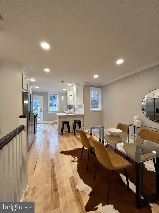 dining space with sink, light wood-type flooring, and crown molding