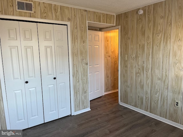 unfurnished bedroom with ornamental molding, a textured ceiling, dark hardwood / wood-style flooring, a closet, and wood walls