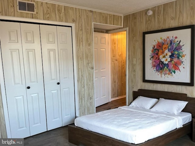 bedroom with wooden walls, a textured ceiling, dark hardwood / wood-style flooring, and a closet