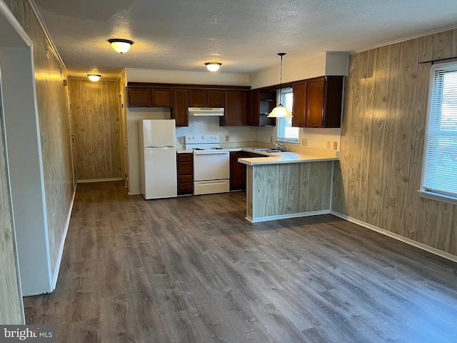 kitchen featuring sink, kitchen peninsula, pendant lighting, white appliances, and wooden walls