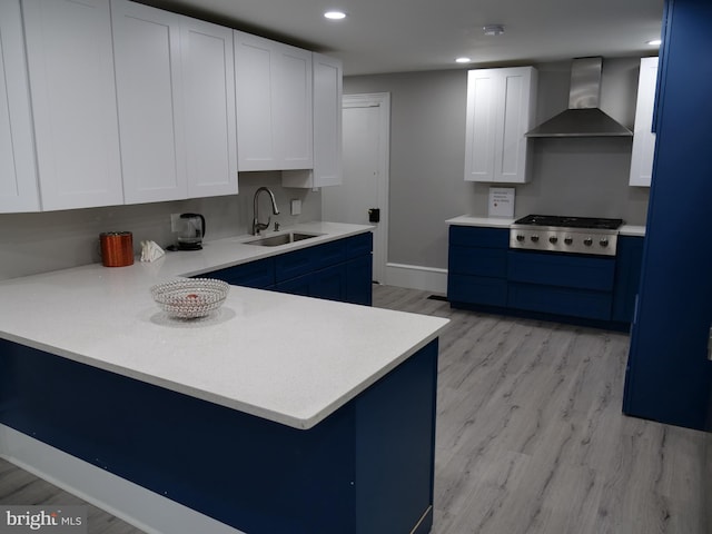 kitchen featuring white cabinetry, sink, wall chimney exhaust hood, stainless steel gas cooktop, and light hardwood / wood-style floors