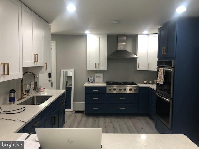 kitchen featuring sink, wall chimney range hood, light hardwood / wood-style flooring, white cabinetry, and stainless steel gas stovetop