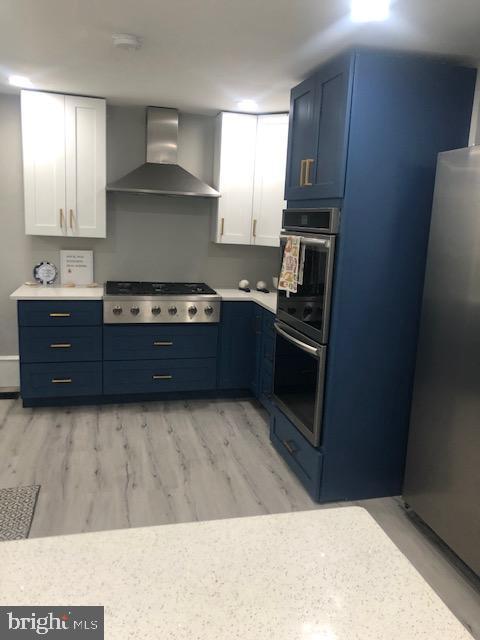 kitchen with light hardwood / wood-style flooring, stainless steel appliances, white cabinetry, and wall chimney range hood