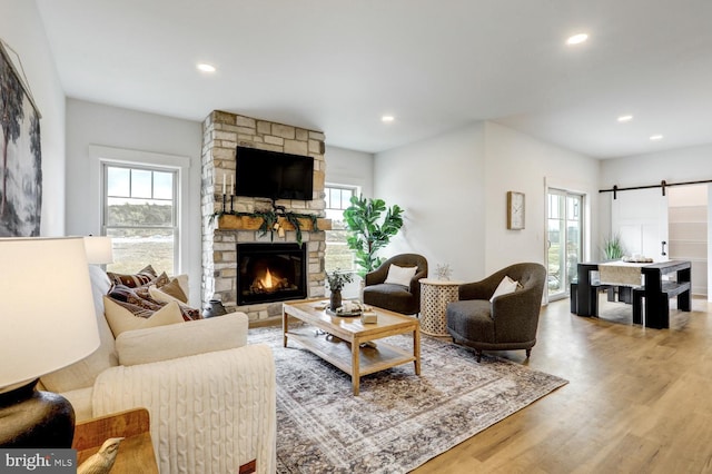 living room featuring hardwood / wood-style flooring, a stone fireplace, and a barn door