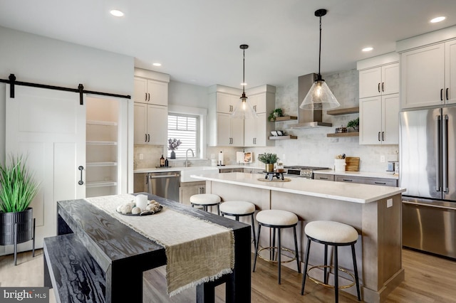 kitchen featuring a kitchen island, pendant lighting, stainless steel appliances, a barn door, and wall chimney range hood