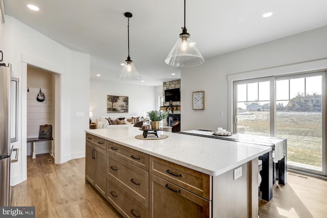 kitchen with a stone fireplace, light hardwood / wood-style flooring, stainless steel refrigerator, a kitchen island, and pendant lighting