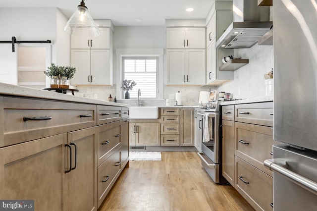 kitchen featuring stainless steel stove, sink, hanging light fixtures, fridge, and wall chimney exhaust hood