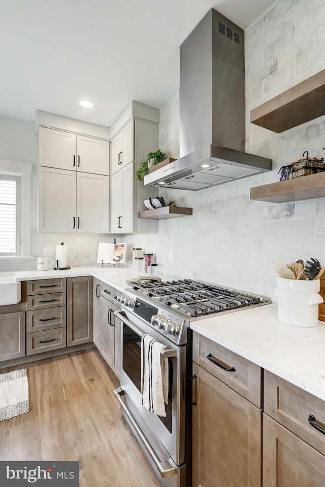 kitchen featuring light stone countertops, gas stove, decorative backsplash, exhaust hood, and light wood-type flooring