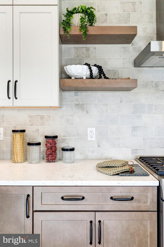 kitchen with light stone counters, wall chimney exhaust hood, stainless steel range with gas stovetop, and backsplash