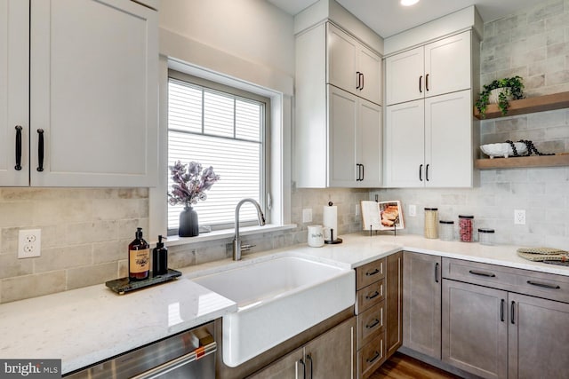 kitchen with light stone counters, stainless steel dishwasher, sink, and backsplash